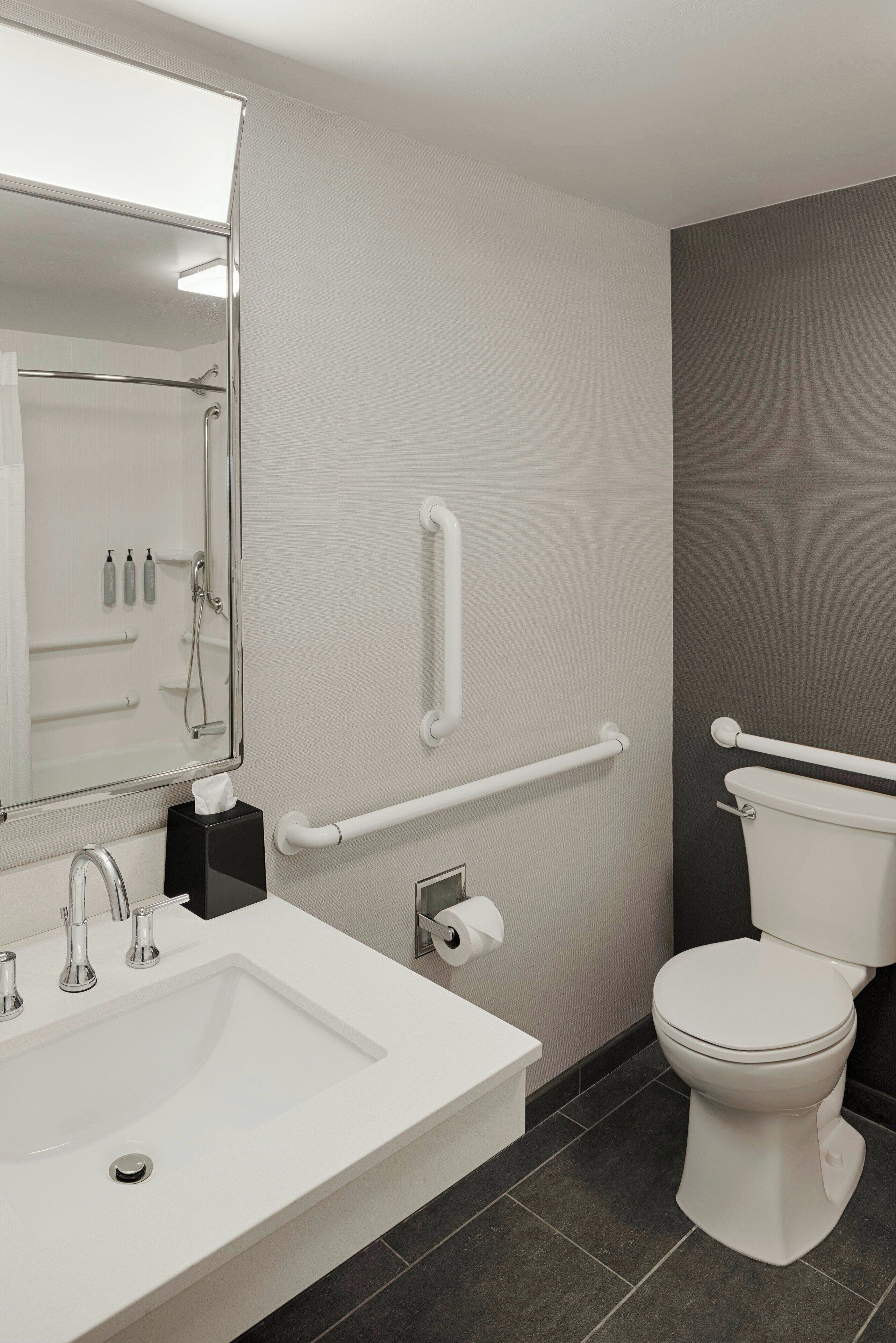 Ein modernes Badezimmer mit Waschbecken, Spiegel, Toilette und Haltestange.