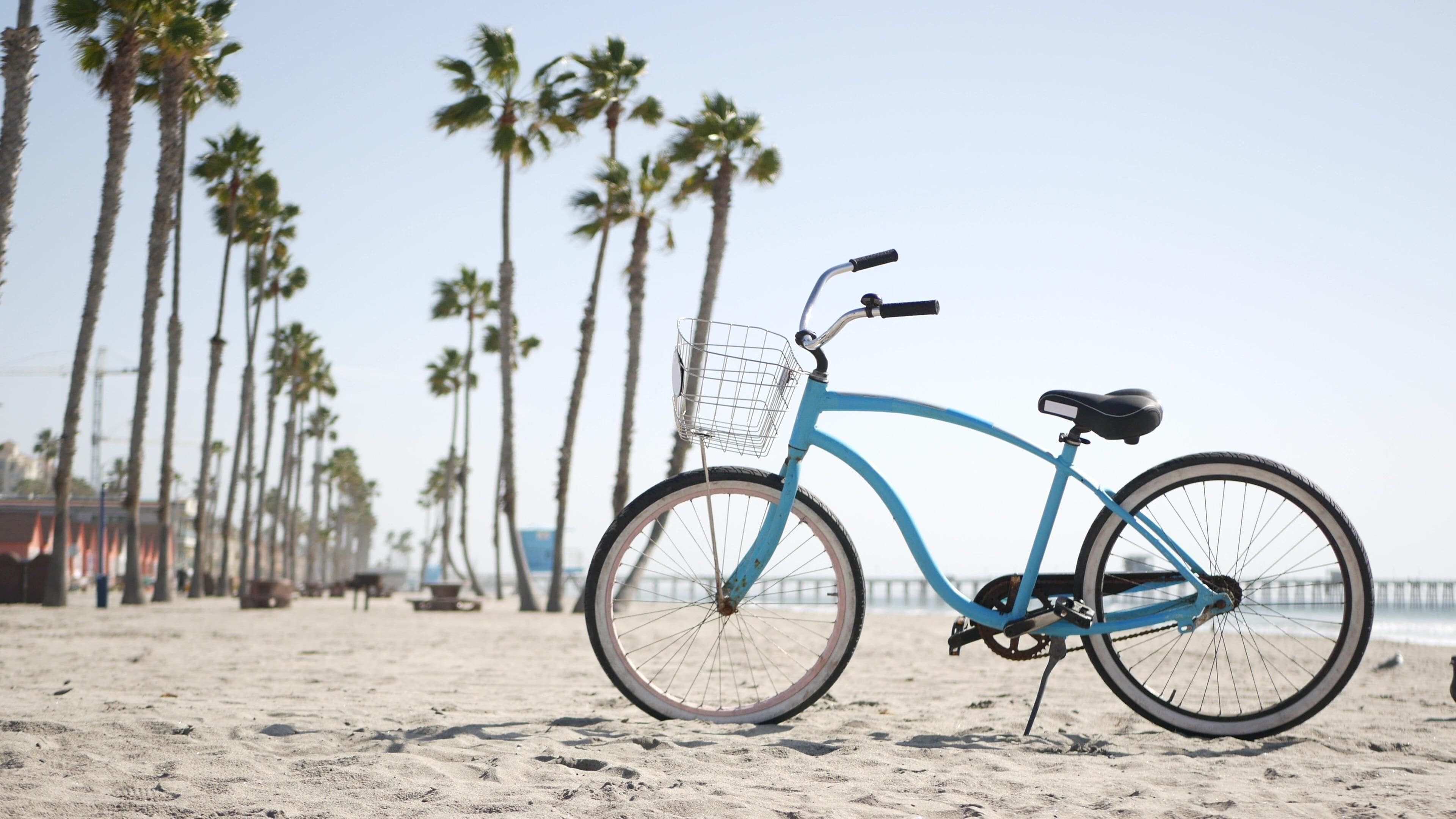 Una bicicleta con una cesta sobre una playa arenosa, con palmeras al fondo.