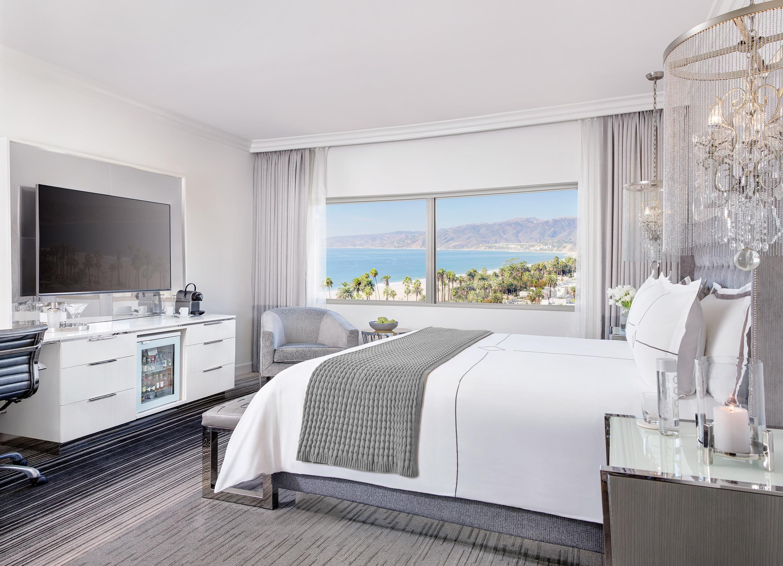 Habitación de hotel moderna con una cama grande, un escritorio con televisor de pantalla plana, minibar y vistas al océano.