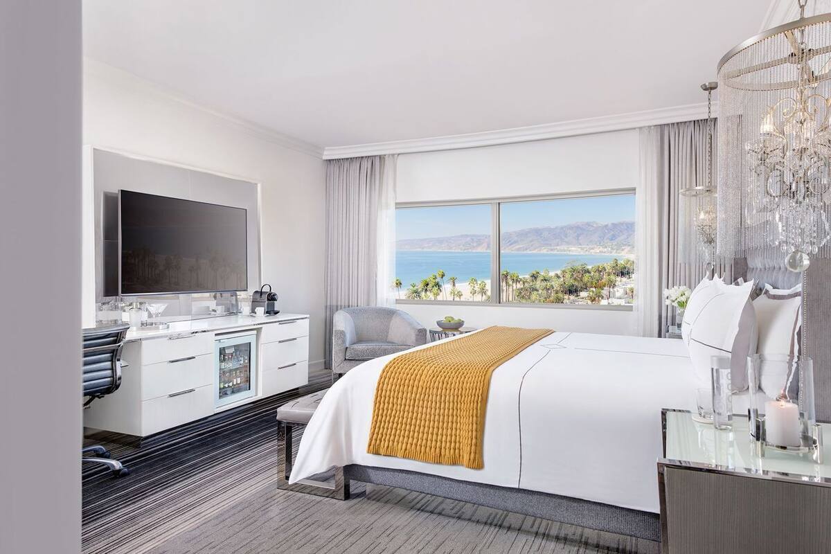 A hotel room with a bed, a desk, a television, and a view of the ocean.