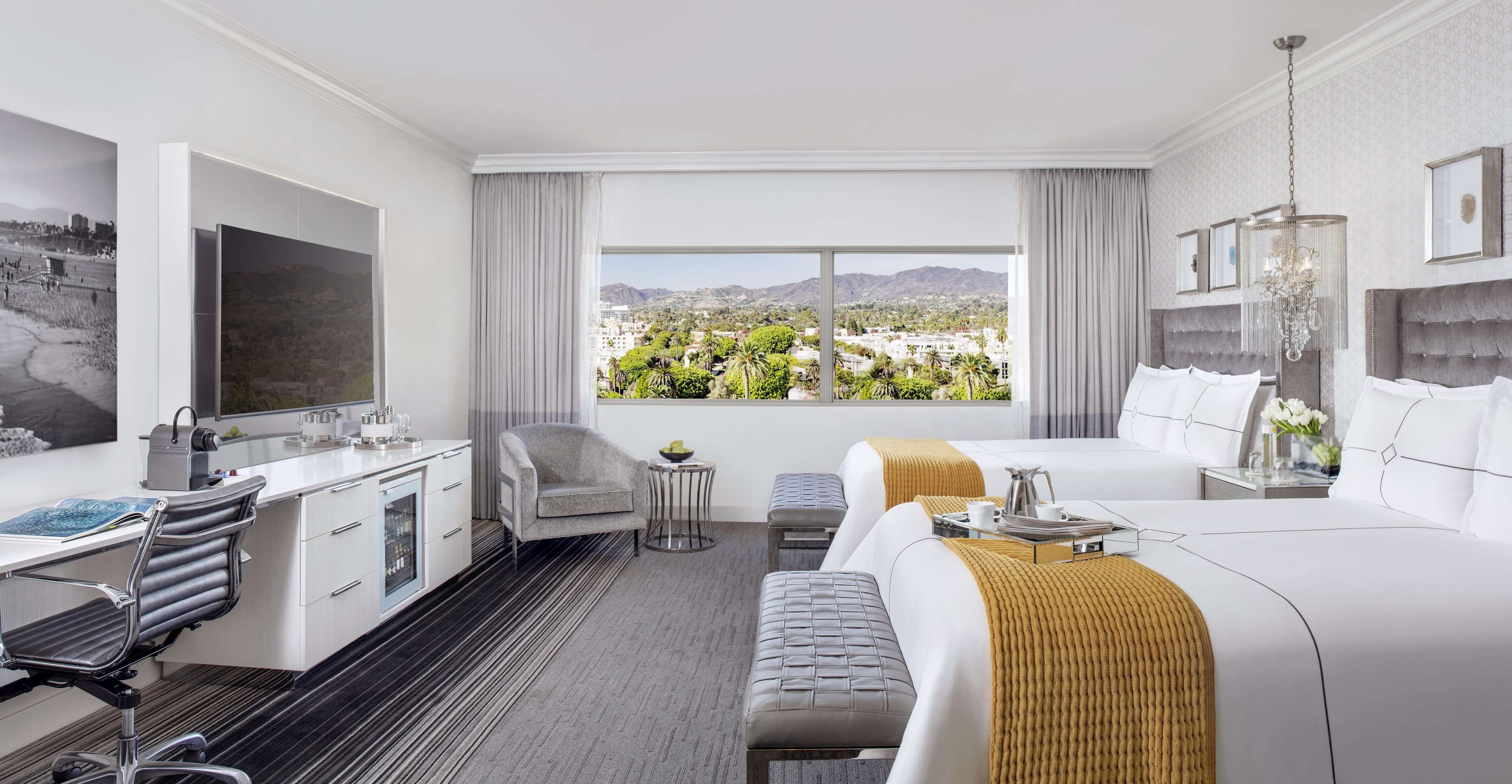 Een hotelkamer met een groot bed, een bureau met stoel, een televisie en uitzicht op een stadsbeeld.