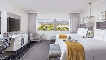 Een hotelkamer met een groot bed, een bureau met stoel, een televisie en uitzicht op een stadsbeeld.