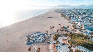 Vista aérea de una playa con un parque de skate, palmeras y un paisaje urbano al fondo.