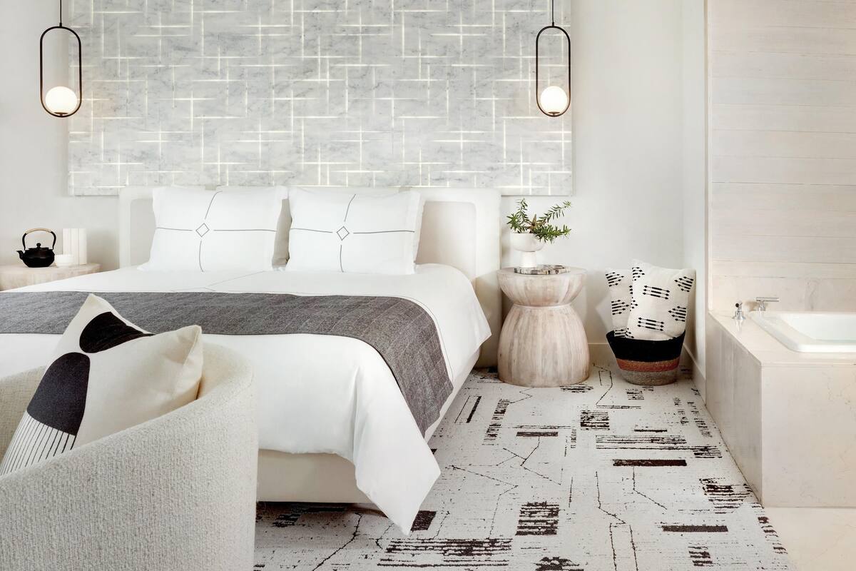 A modern bedroom with a large bed, two bedside tables, a nightstand, a wall-mounted light fixture, and a patterned floor.