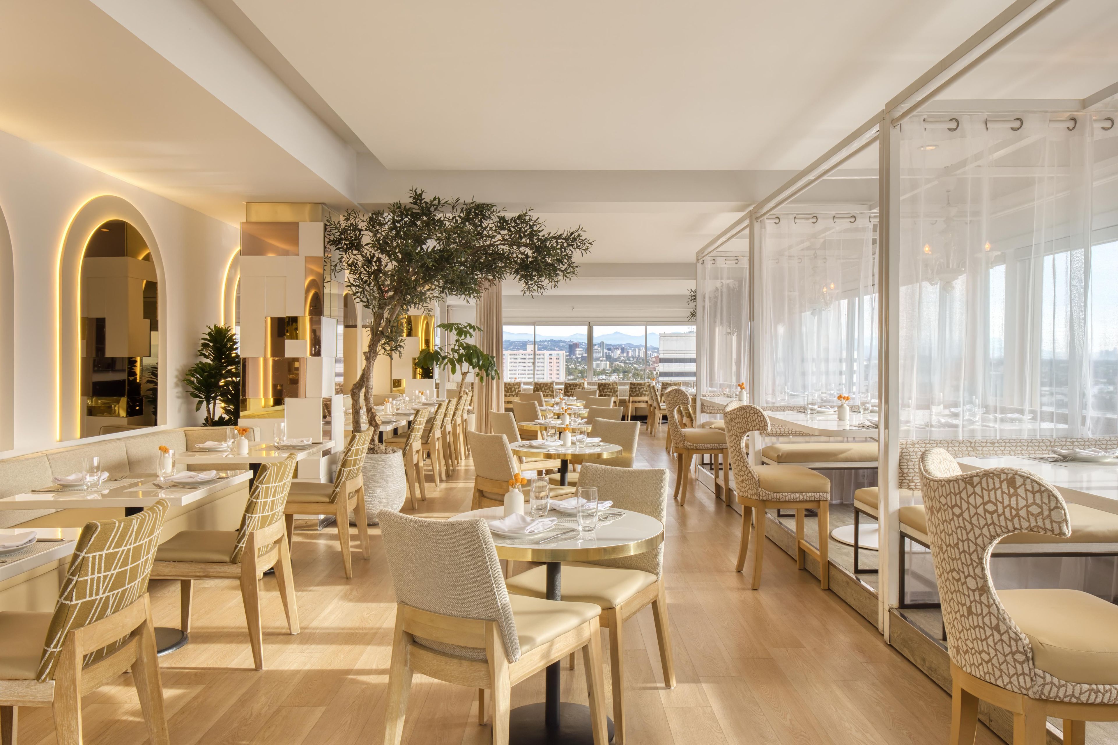 Un restaurante moderno con techos altos, amplias ventanas y vistas a la ciudad.