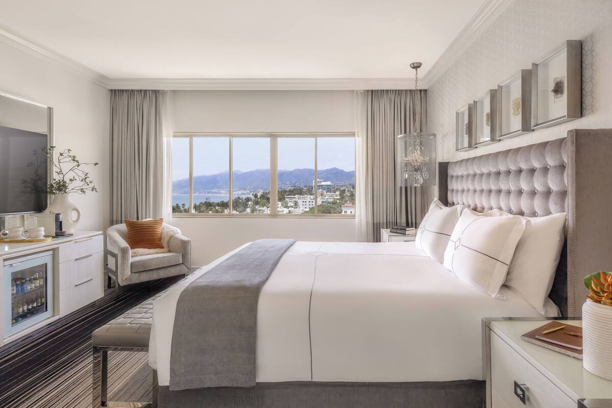 A hotel room with a large bed, a TV, a desk, and a view of the city.