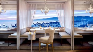 Un comedor con vistas al mar y al paisaje urbano, con una mesa para dos, champán y copas.