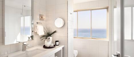 Un baño moderno con un espejo grande, azulejos blancos, un lavabo y una ventana con vistas al mar.