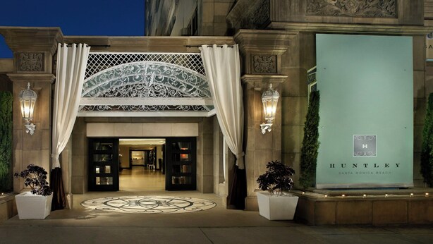 La entrada de un hotel con un dosel ornamentado y un letrero grande que dice 'HUNTLEY SANTA MONICA BEACH'.