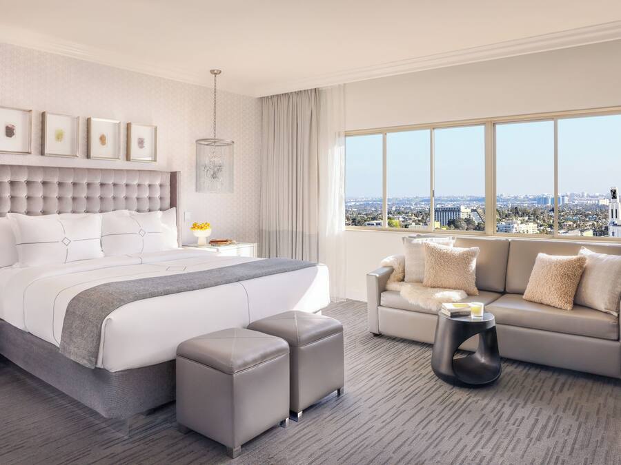 A modern hotel room with a large bed, a sofa, and a view of the city.