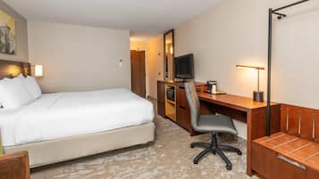 A hotel room with a bed, a desk with a chair, a television, and a desk lamp.