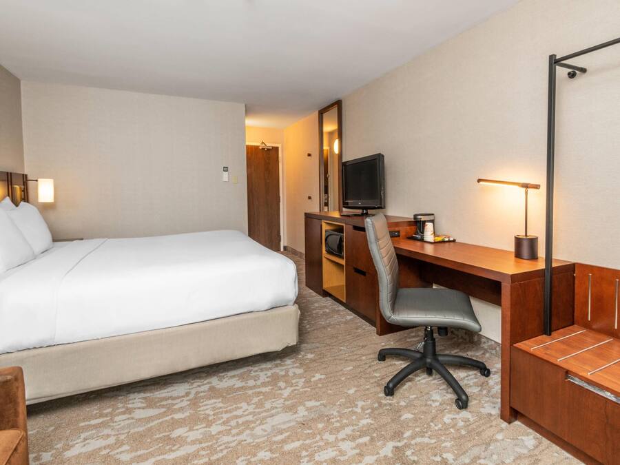 A hotel room with a bed, a desk with a chair, a television, and a desk lamp.