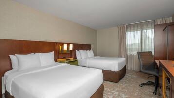 A hotel room with two beds, a desk, a chair, a nightstand, and a window with curtains.