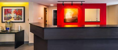 A reception area with a dark reception desk, a framed painting on the wall, and a red accent wall with a large mirror.