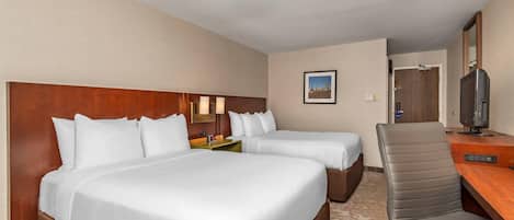 A hotel room with two beds, a desk, a chair, a television, and a framed picture on the wall.