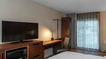 Een hotelkamer met een flatscreen televisie, een magnetron, een bureau, een stoel en een groot raam met gordijnen.