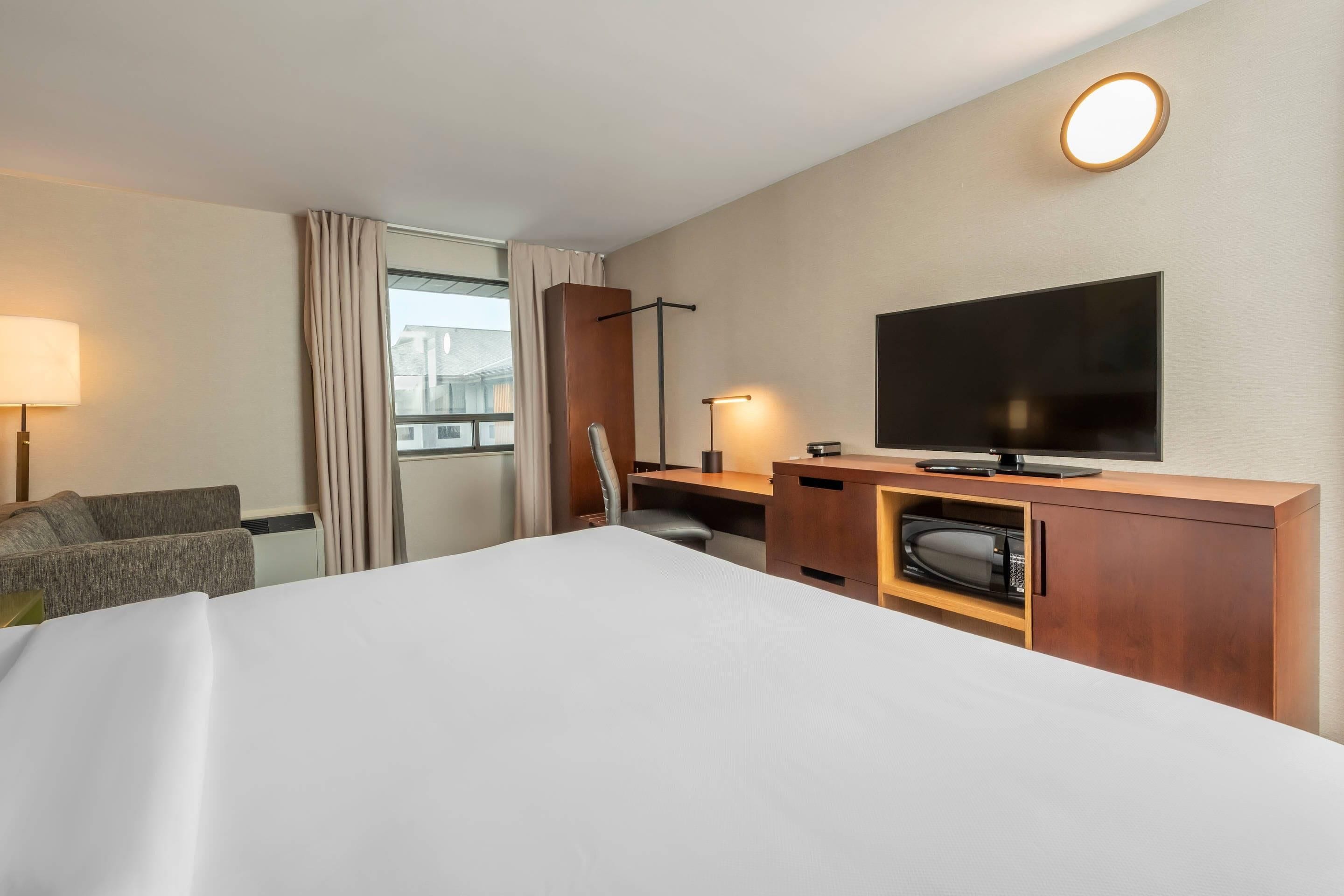 A hotel room with a bed, a desk with a flat-screen TV, a microwave, a lamp, and a sofa.