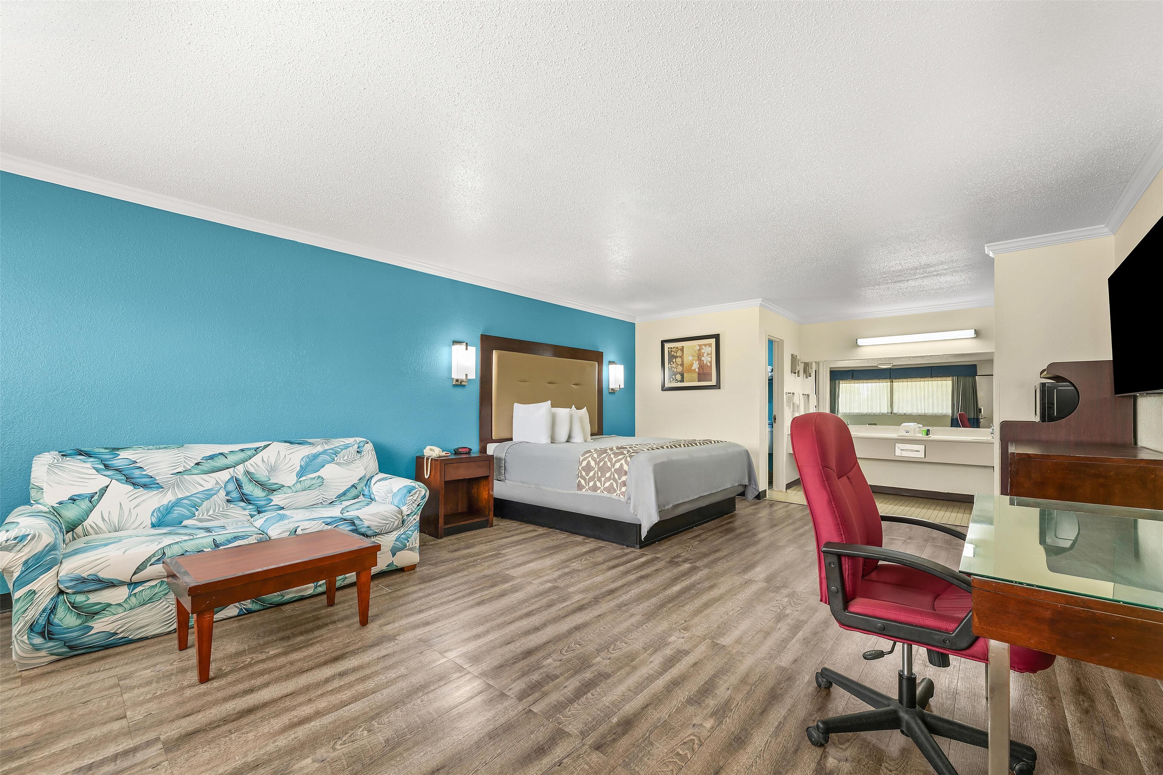 A hotel room with a bed, a desk, a chair, a sofa, and a small table.