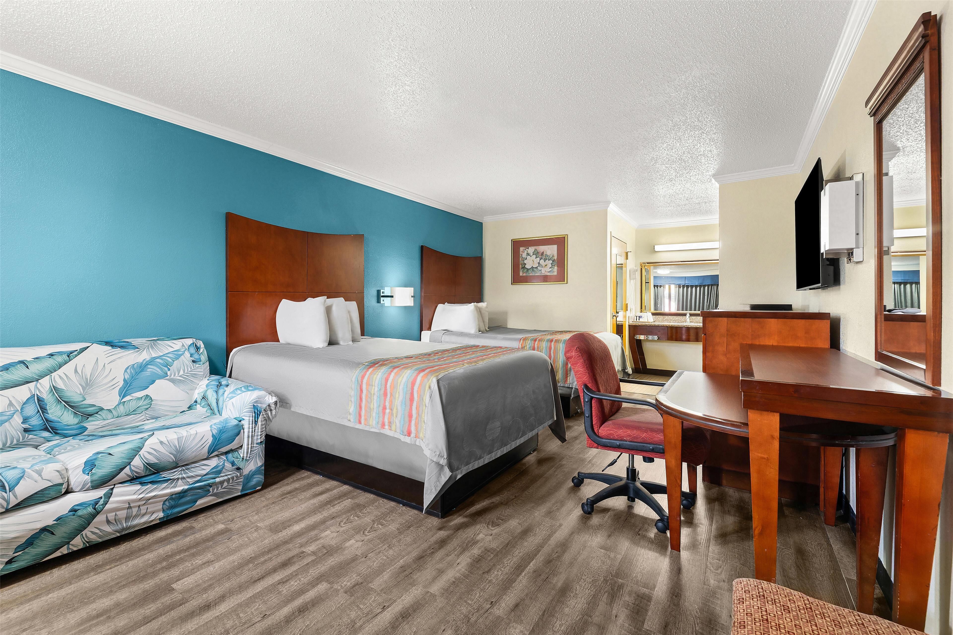 A hotel room with two beds, a desk, a chair, and a sofa.
