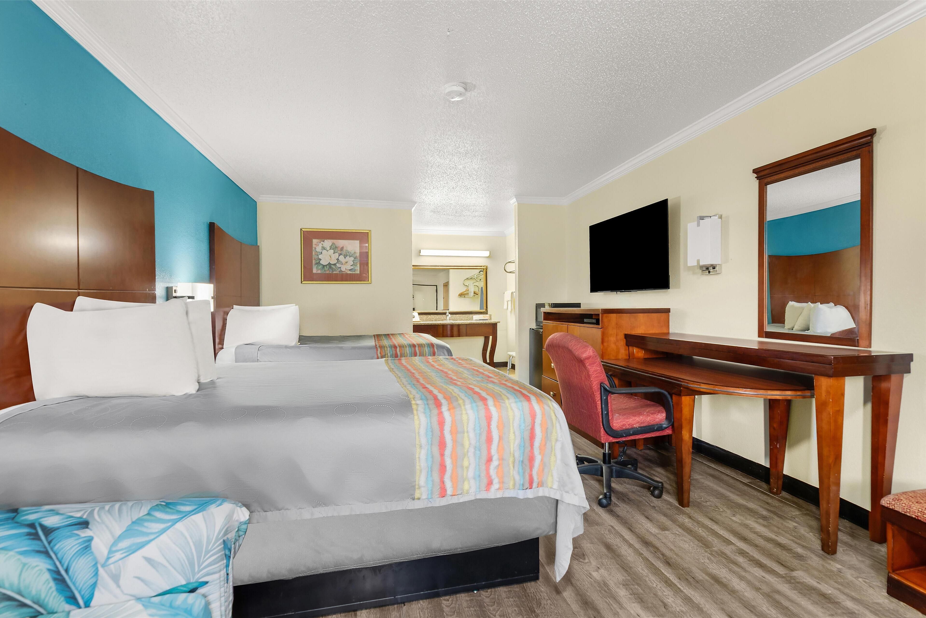 A hotel room with a large bed, a desk, a chair, a television, and a mirror.