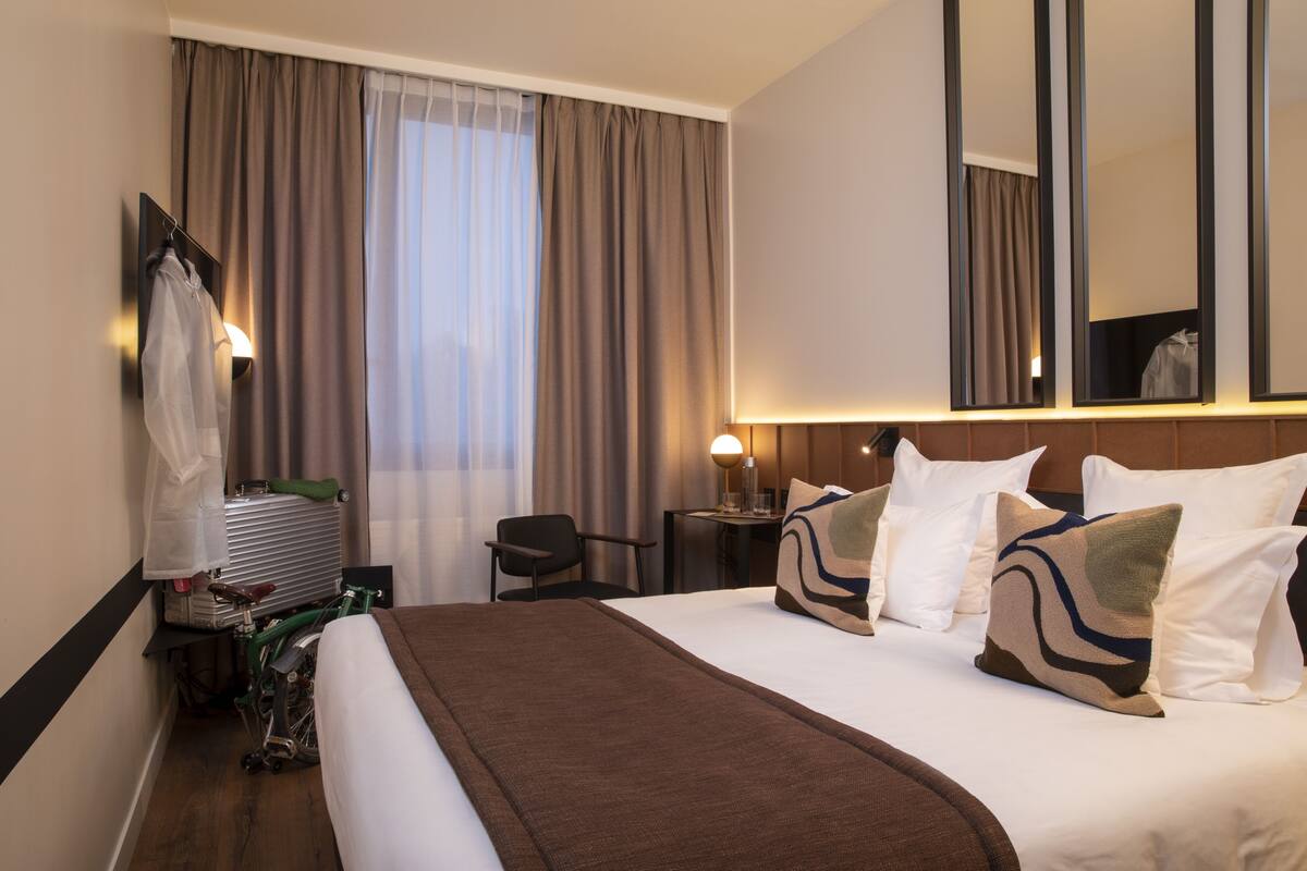 A hotel room with a large bed, a chair, a desk, a bicycle, and a mirror.