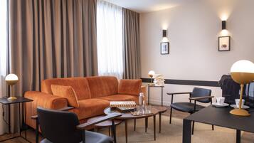 A modern hotel room with a sofa, two armchairs, a coffee table, and a side table with a lamp and a picture frame.