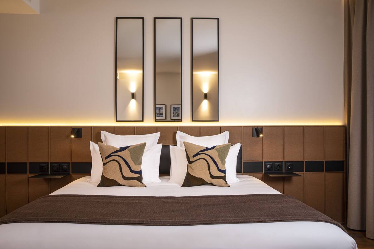 A hotel room with a large bed, three wall-mounted mirrors, and bedside lamps.