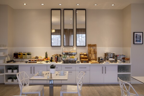 A modern kitchen with white cabinetry, a breakfast bar, and various food items. - Hotel du Port (Nogent-sur-Marne)