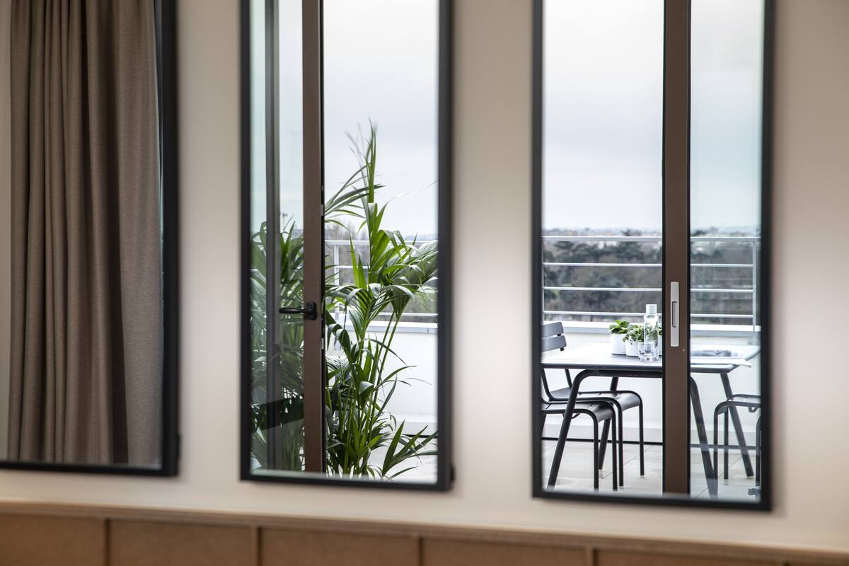 A room with a view of a balcony, a potted plant, and a table with chairs.