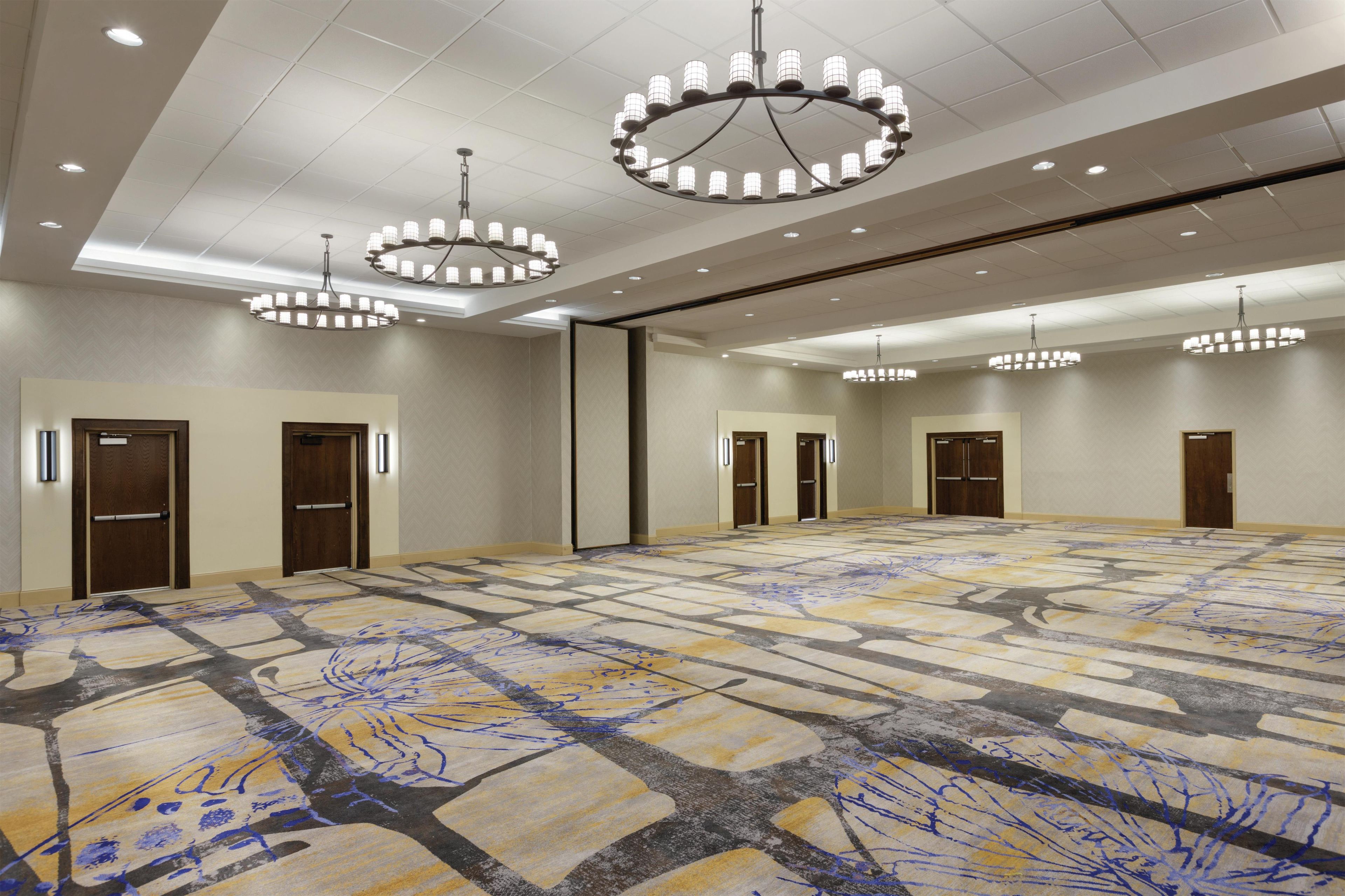 A large conference room with a patterned carpet, multiple doors, and chandeliers.