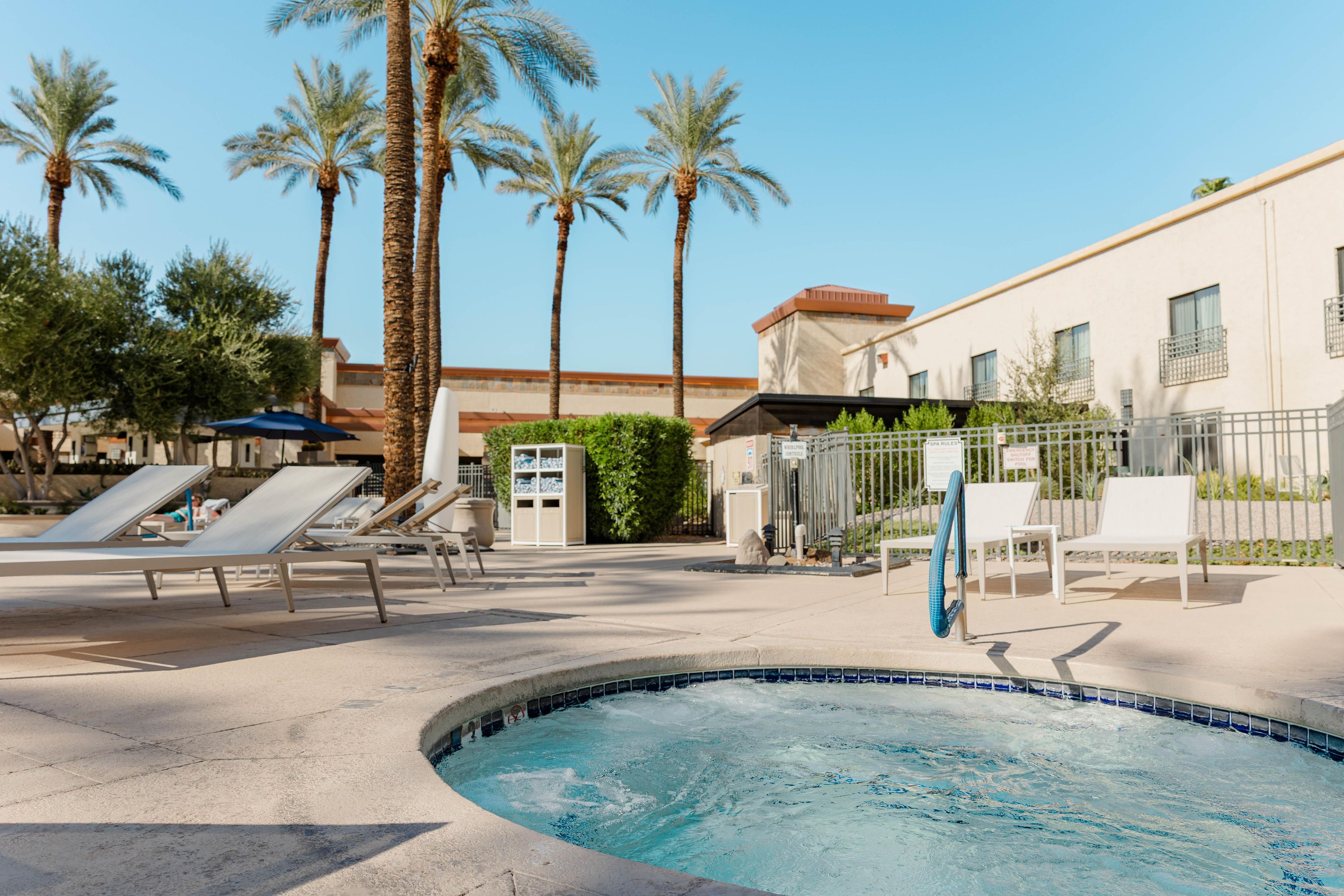 A swimming pool area with lounge chairs, palm trees, and a building with a sign indicating spa rules.