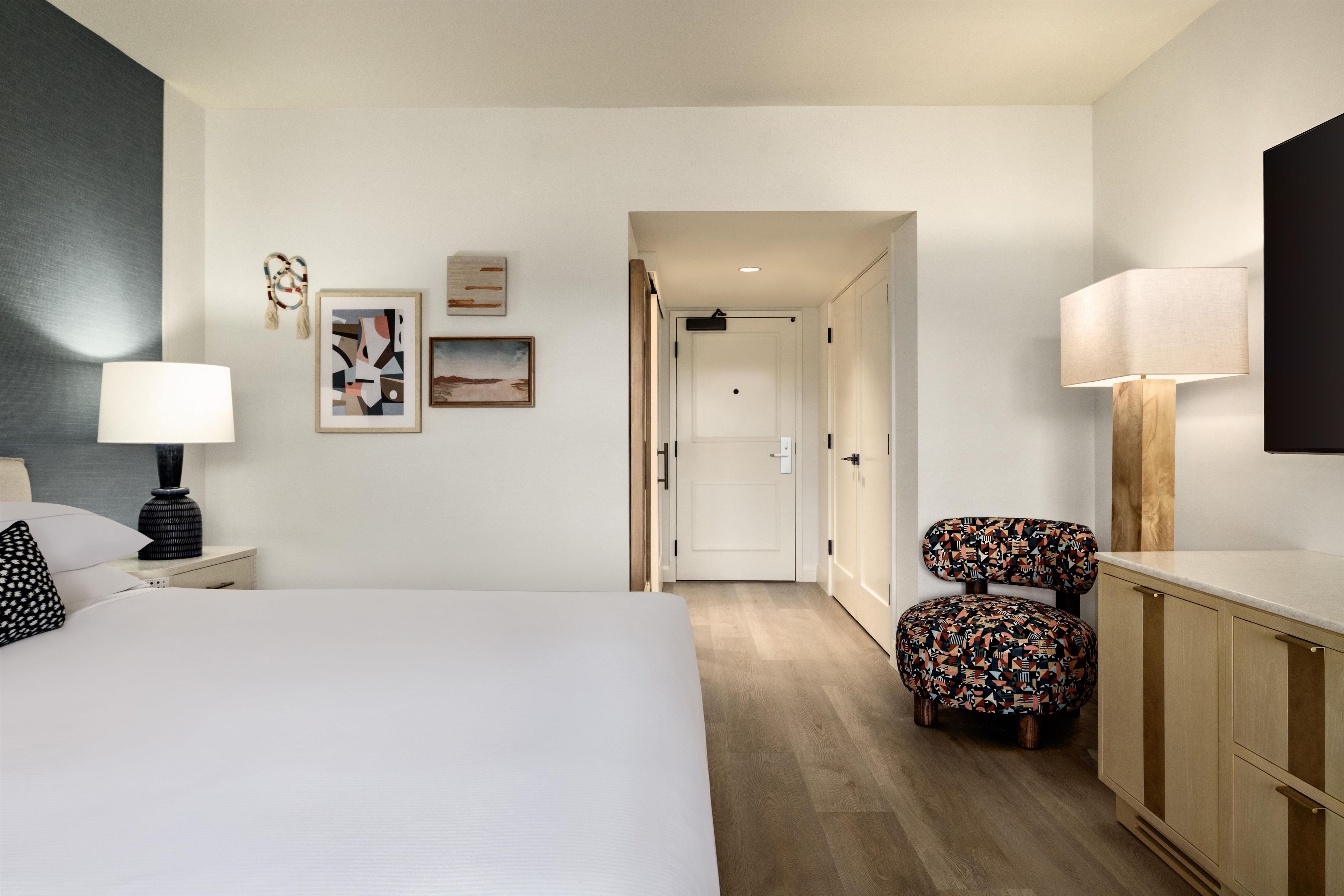 A hotel room with a bed, a chair, a desk, and a wardrobe.