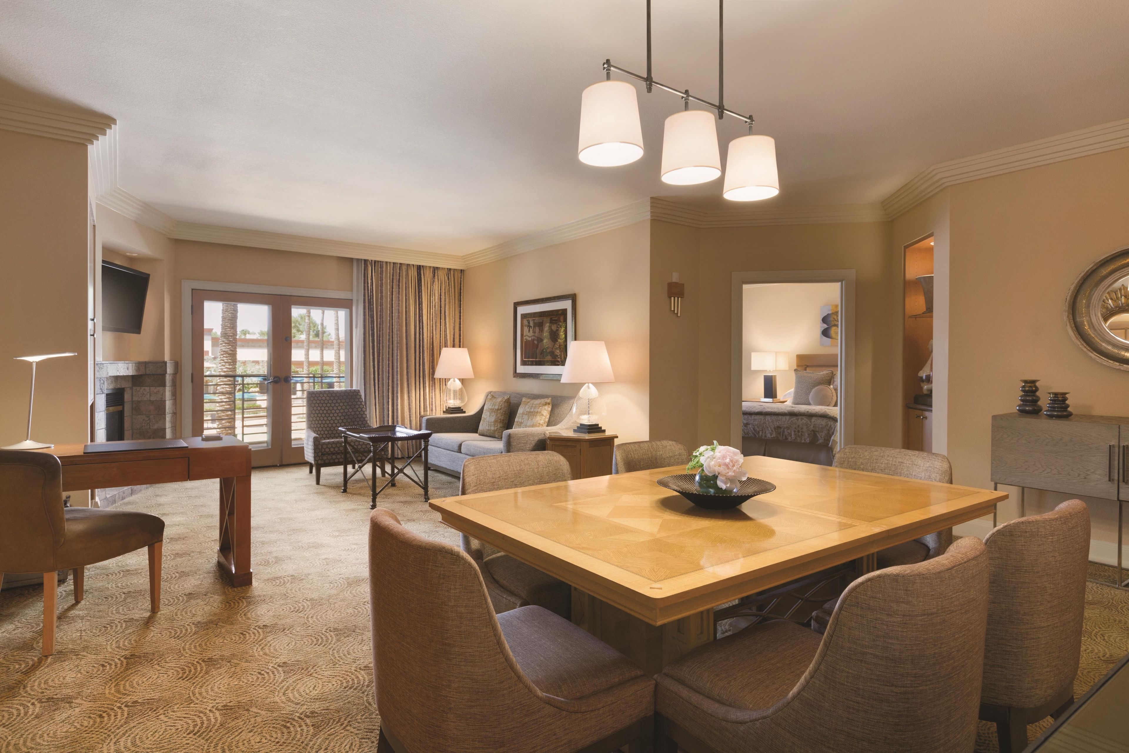 A spacious living area with a wooden dining table, comfortable seating, a flat-screen TV, and a large window with curtains.