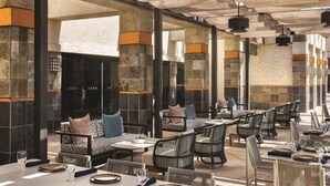 An outdoor dining area with stone columns, cushioned seating, and tables set for dining. - Hilton Scottsdale Resort & Villas (Scottsdale)