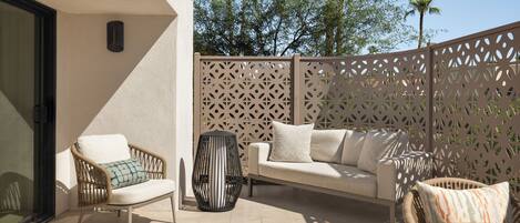 Eine Terrasse im Freien mit einer weißen Couch, Korbstühlen und einem Holztisch.