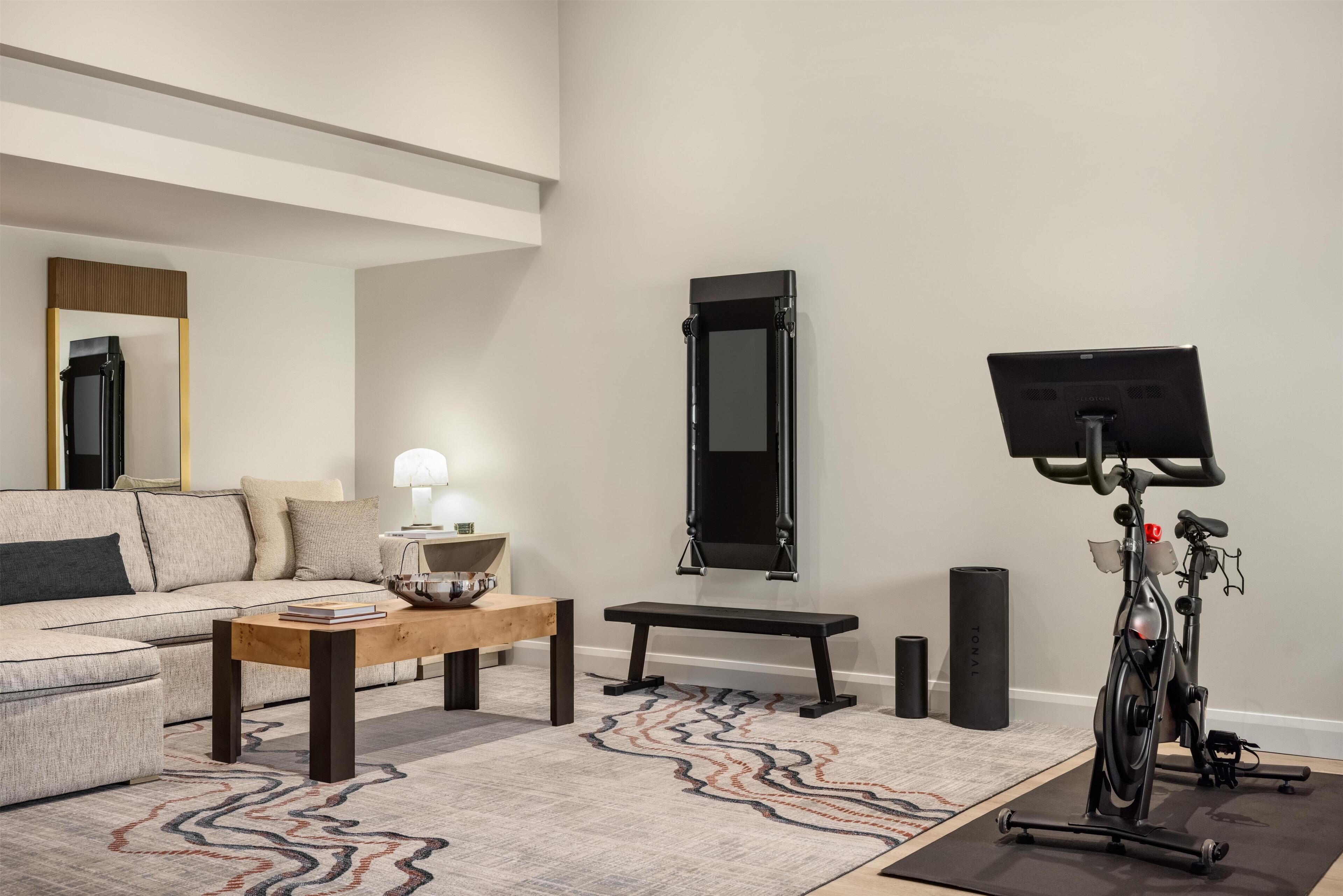 A living room with a sofa, coffee table, bench, exercise bike, and a mirror on the wall.