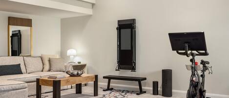 A living room with a sofa, coffee table, bench, exercise bike, and a mirror on the wall.