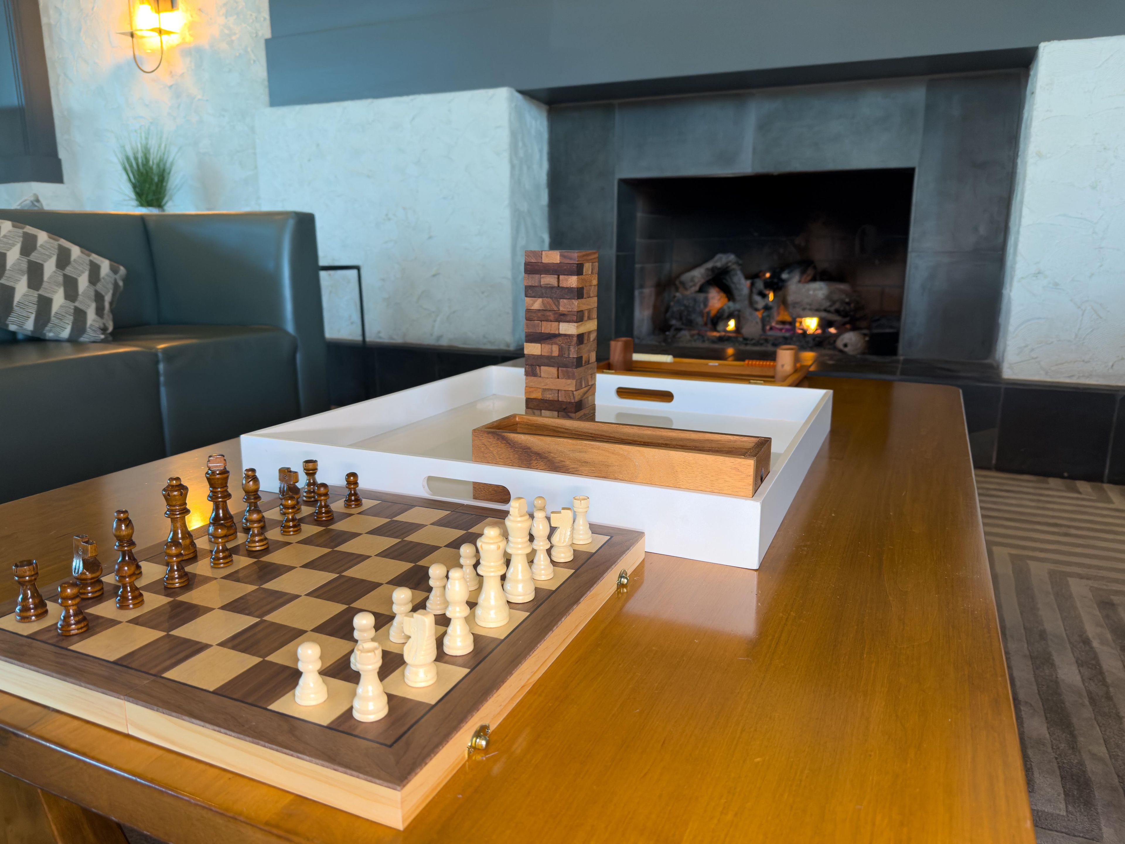 Un jeu d’échecs est posé sur une table en bois, dans une pièce qui comprend une cheminée et un canapé.