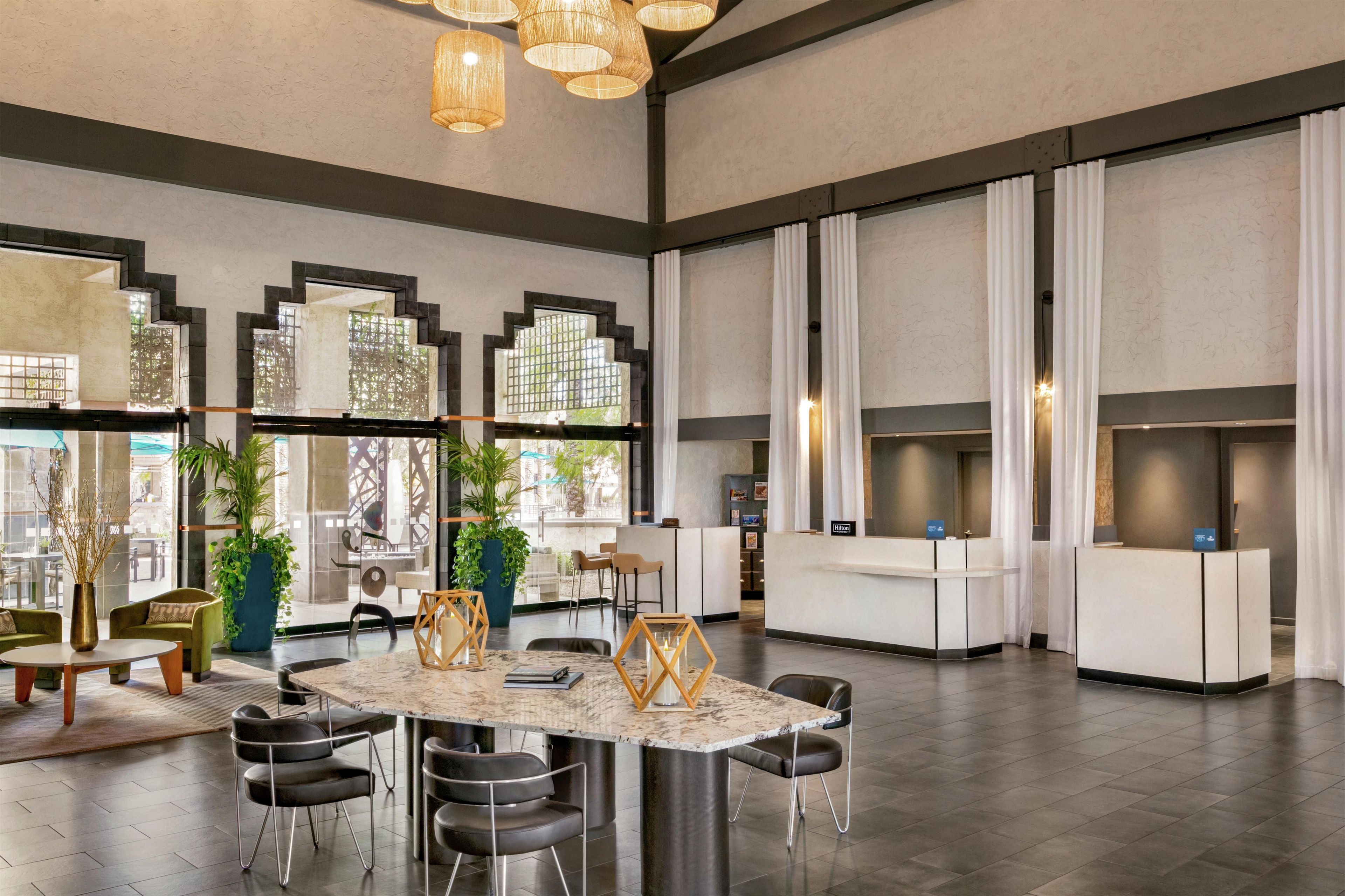A spacious lobby with a marble reception desk, modern chairs, and large windows with curtains.