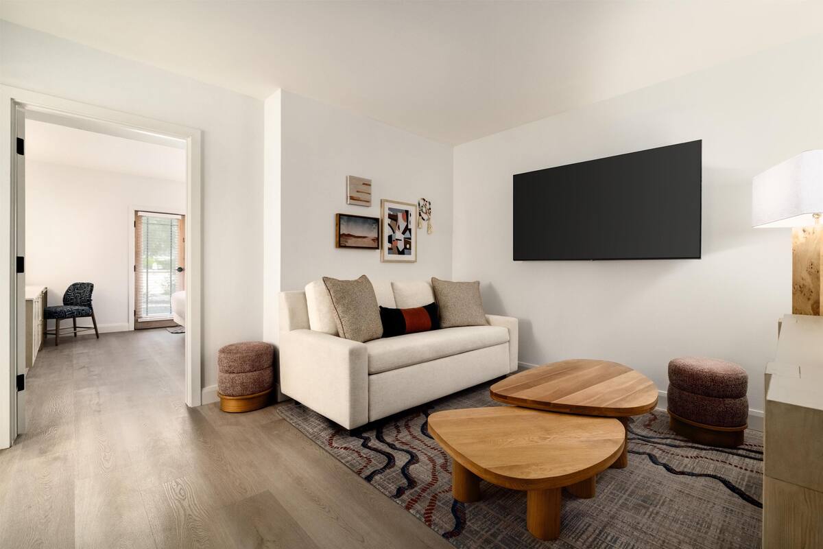 A modern living room with a sofa, two wooden side tables, a flat-screen TV, and a patterned rug.