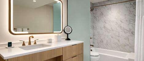 A modern bathroom with a large mirror, two sinks, a toilet, and a bathtub.