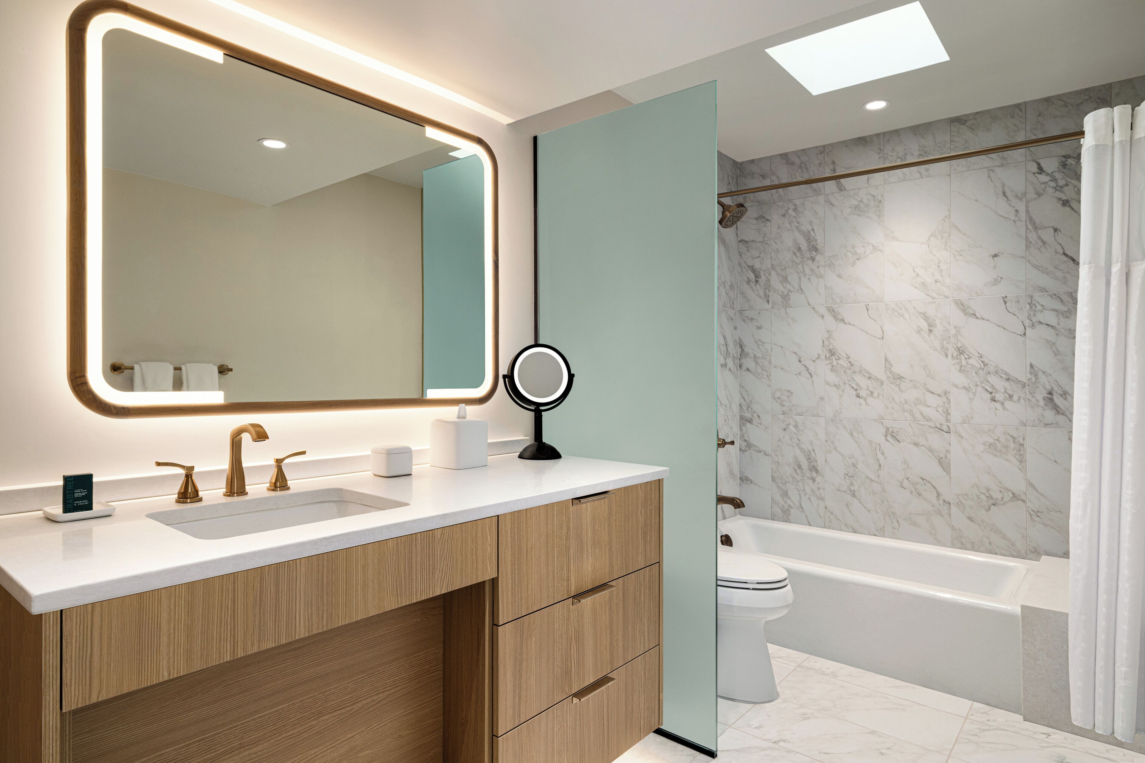 Un bagno moderno con uno specchio grande, due lavabi, un mobile contenitore con cassetti, un water e una vasca da bagno.