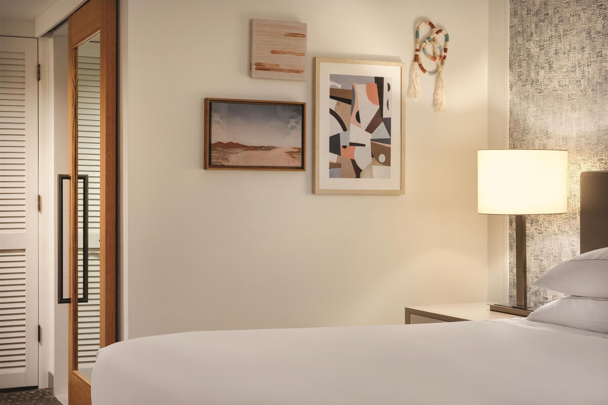 A hotel room with a bed, a nightstand, a lamp, and wall art.
