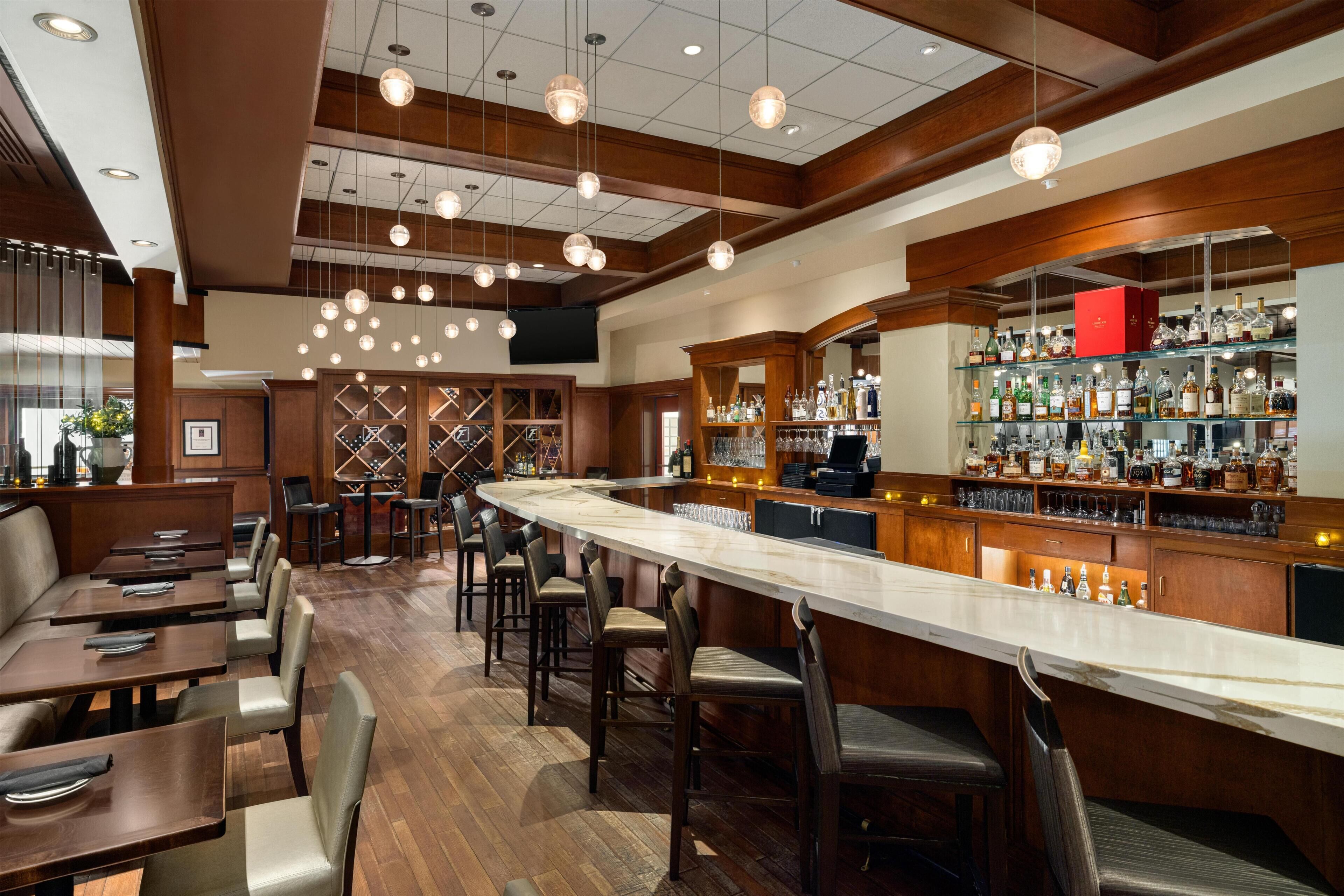 A bar area with a long counter, multiple seating options, and a well-stocked liquor display.