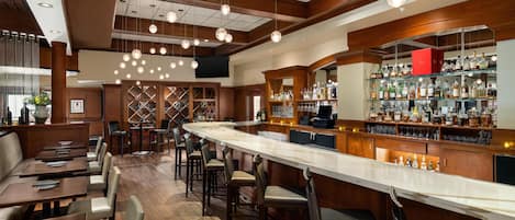 A bar area with a long counter, multiple seating options, and a well-stocked liquor display.