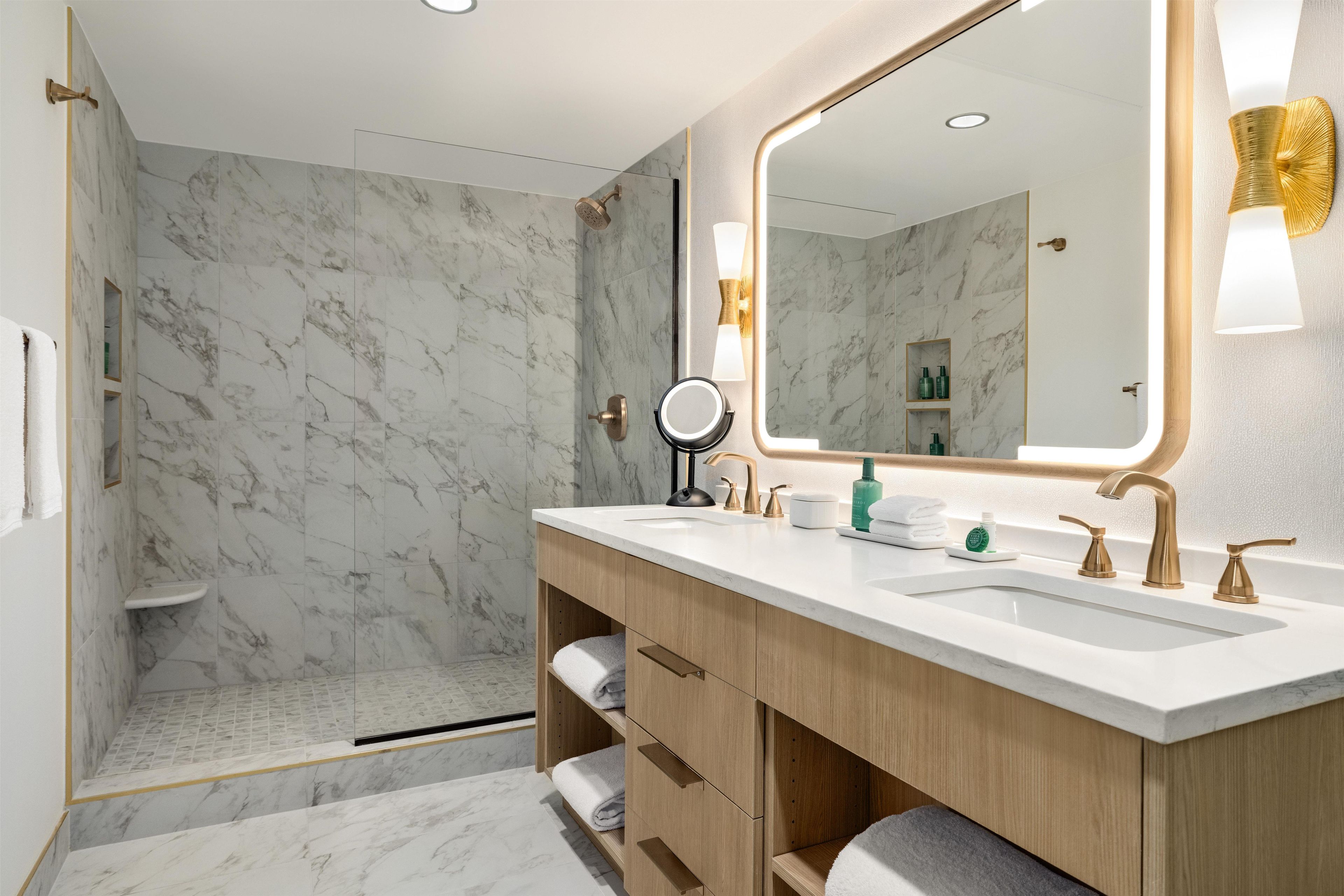 A modern bathroom with a marble shower, a large mirror, and a vanity with a sink and multiple faucets.