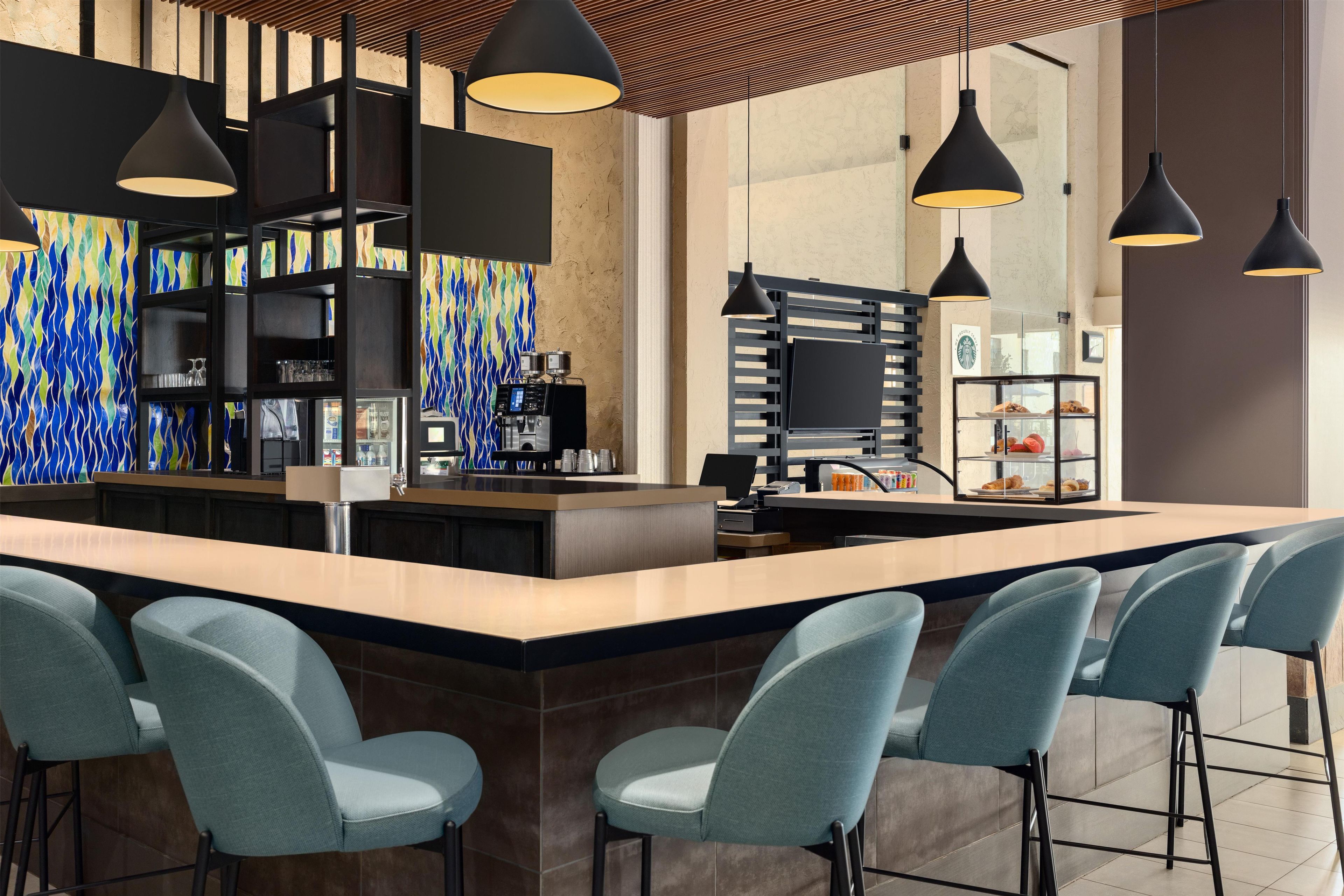 A modern bar area with a central island, bar stools, pendant lighting, and a colorful abstract wall.