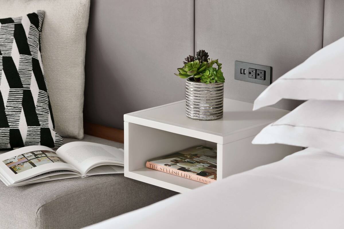 A neatly arranged bedside table with a book, a decorative vase with a succulent plant, and a power outlet.
