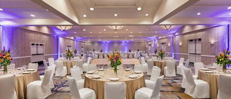 Un amplio salón de conferencias con mesas redondas, sillas blancas y centros de mesa florales.