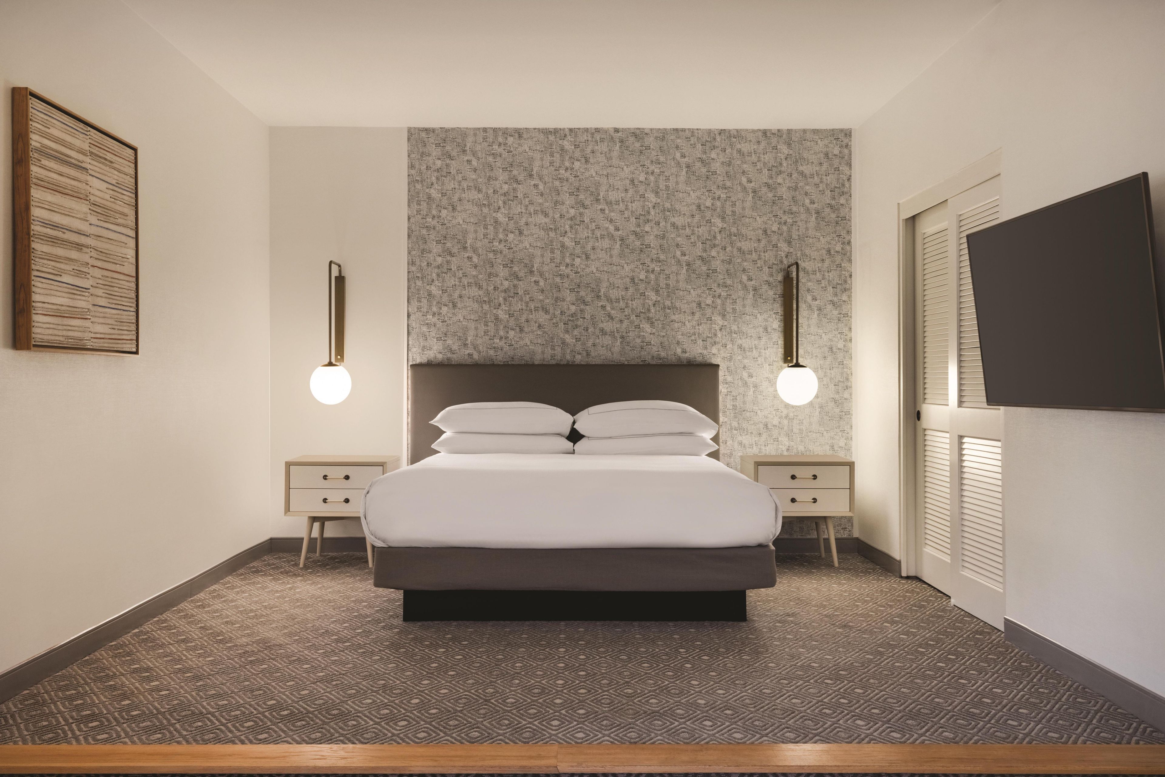 A modern bedroom with a large bed, two bedside tables, a wall-mounted TV, and patterned wallpaper.